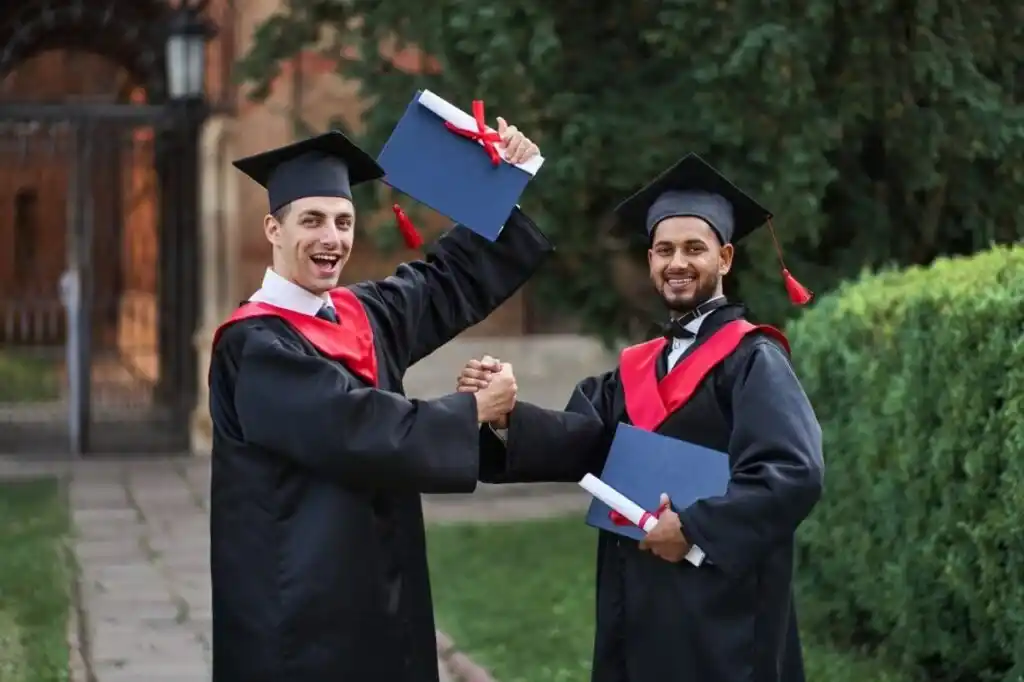 Two graduates in caps and gowns celebrate by shaking hands.