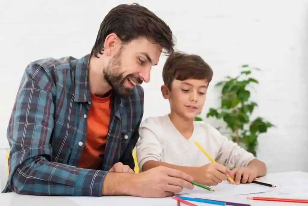 A man and a boy are engaged in a drawing activity, surrounded by colorful pencils on a bright, white tabletop.