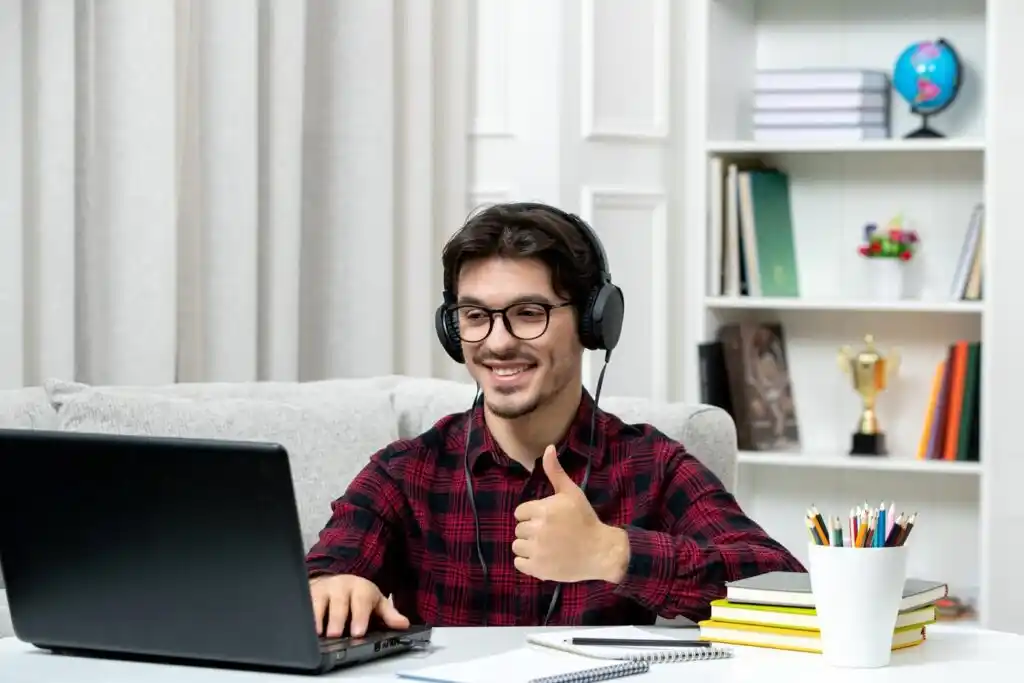 person in a checkered shirt and headphones sits at a desk with a laptop