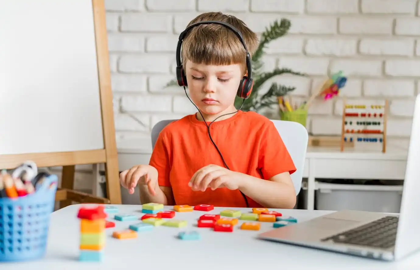 child wearing headphones sits at a table, playing with colorful building