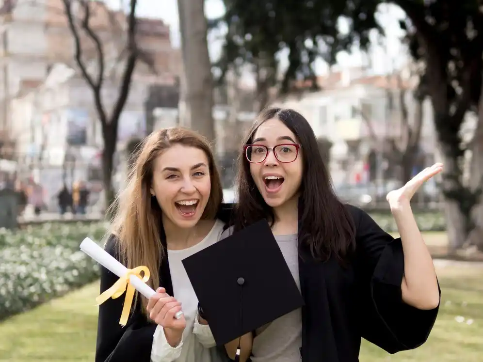One holding a diploma with a yellow ribbon, while the other gestures joyfully.