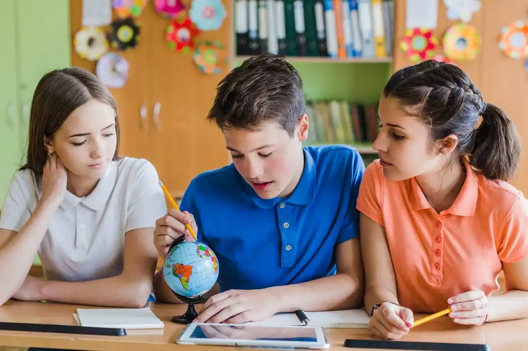 Three students engaged in a study session with a globe and tablet on the table.