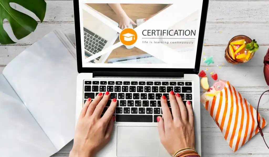 laptop displaying a certification logo, with hands typing