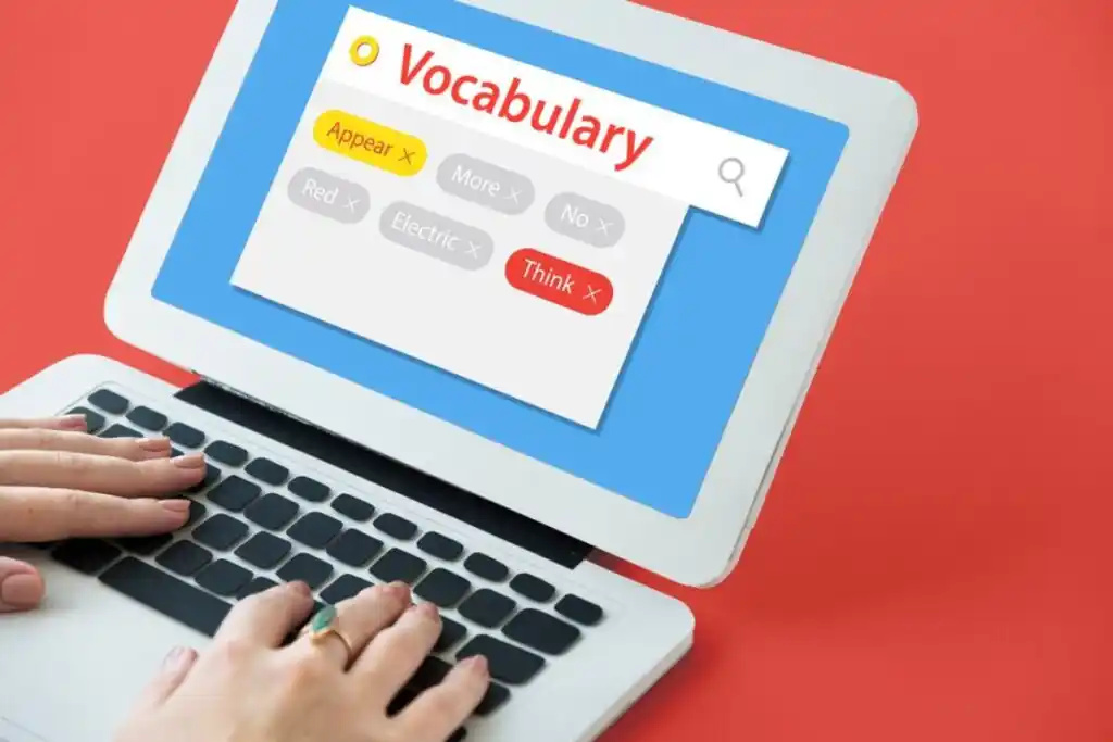 A person's hands typing on a laptop displaying a colorful vocabulary search interface with various keywords highlighted.