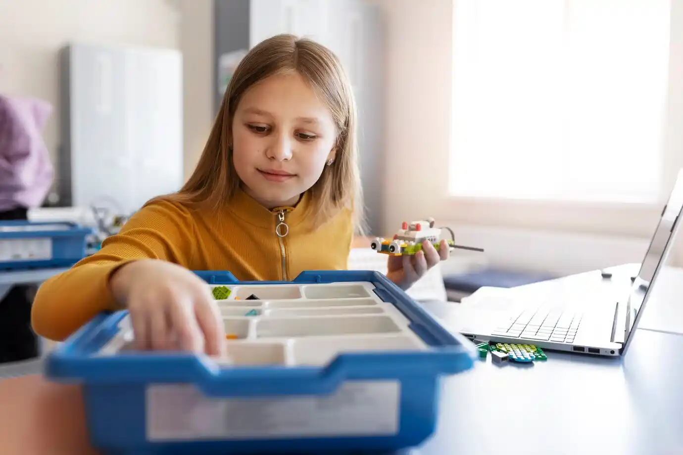 girl using a laptop and electronic parts to build a robot