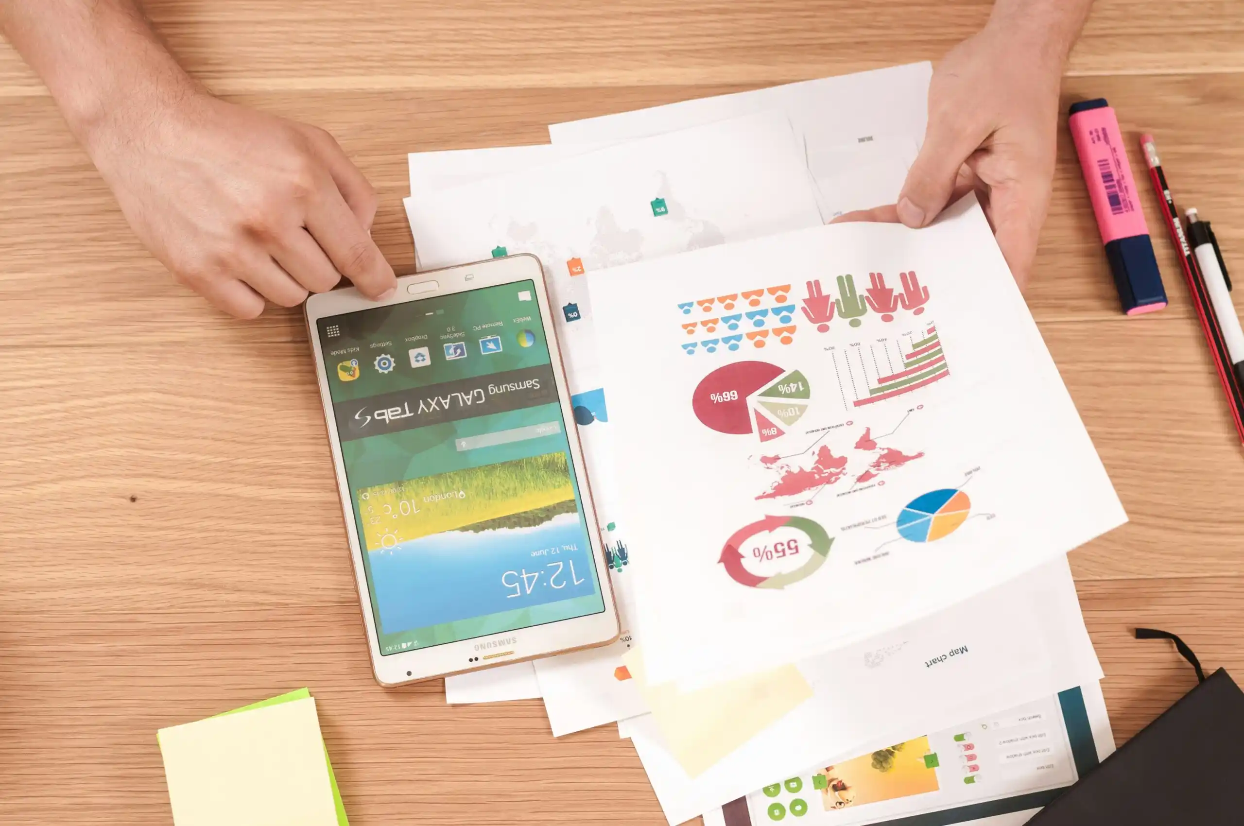 A person's hand holds printed charts and statistics next to a tablet.