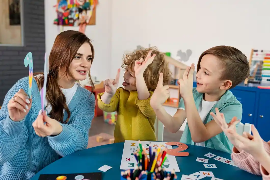 A teacher engages with children at a colorful table, showcasing colorful letters and crafts as they excitedly participate in learning.