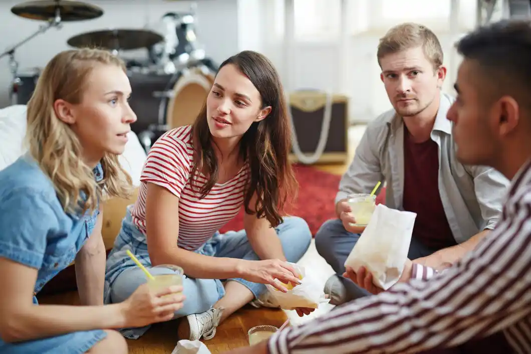  A group of friends sits on the floor, enjoying drinks and snacks, surrounded by musical instruments.