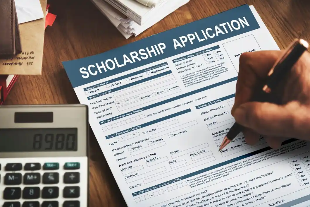 A person filling out a scholarship application form with a pen.
