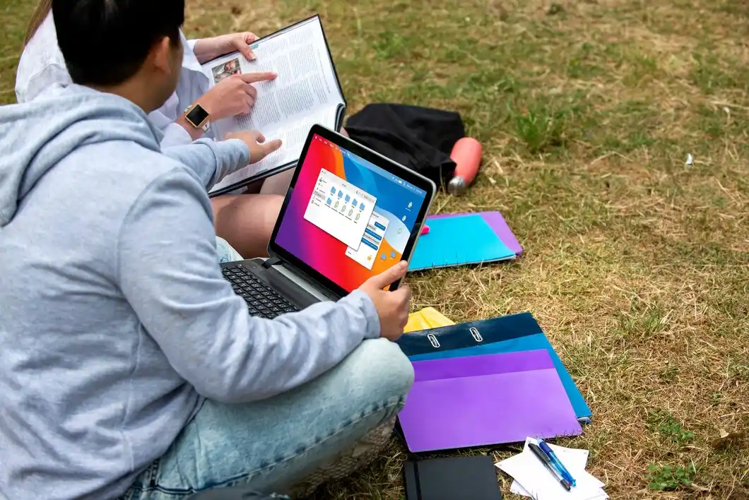 A laptop with a colorful screen, and the other reading a book with students.