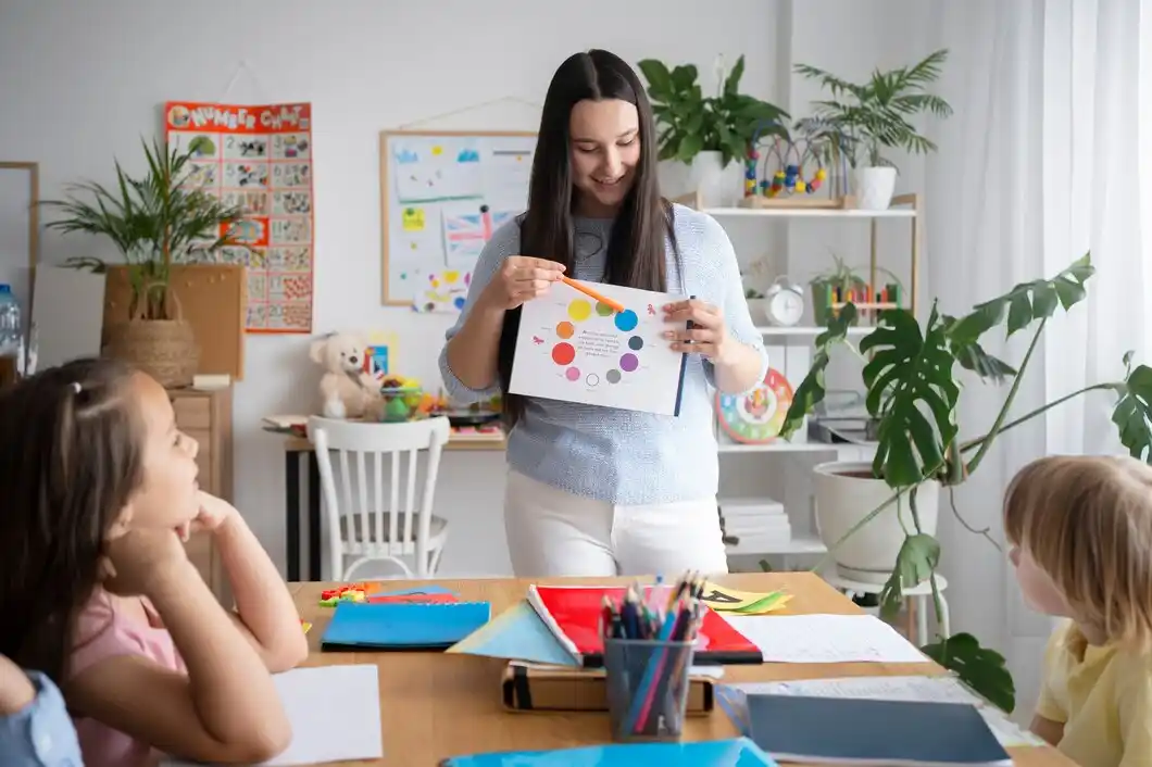 A teacher stands at a table, presenting a colorful educational chart to attentive students.