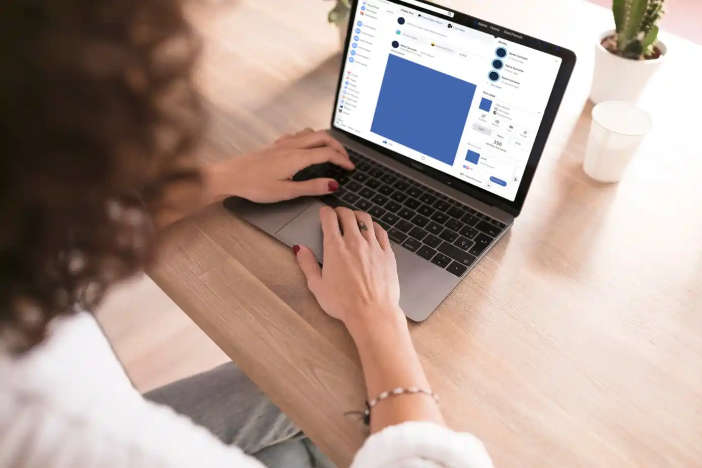  person with curly hair works on a laptop at a wooden table