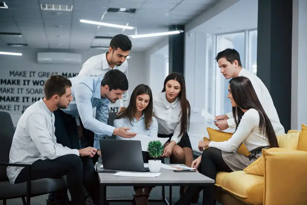 The professionals collaborate around a laptop in a modern office setting, reviewing documents and discussing ideas..