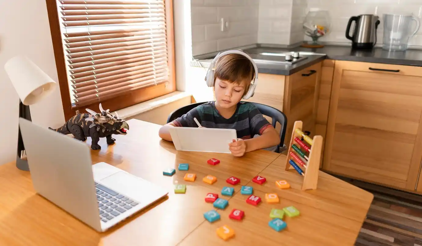 child wearing headphones sits at a wooden desk