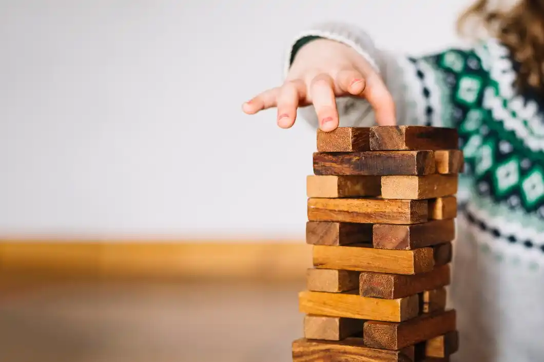 A child's hand reaches for a wooden block in a tall stack,