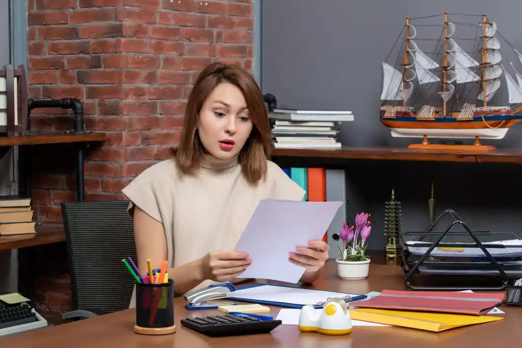 A person in a cozy office reads documents, surrounded by books.