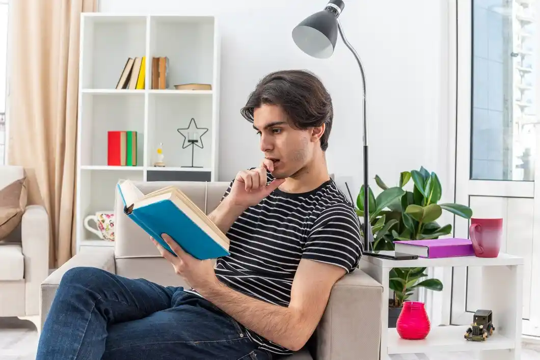 A person sits comfortably on a sofa, reading a blue book in a bright, modern living room with plants and bookshelves.