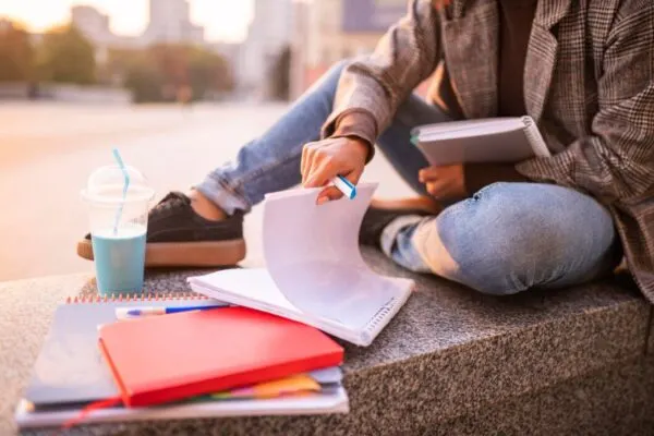 A student sits outside with notebooks, a blue drink, and a pen, reviewing notes.