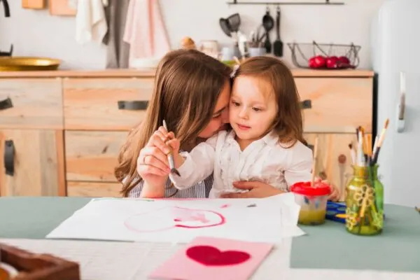 Two young children engaged in drawing, surrounded by art supplies and colorful creations on a table.
